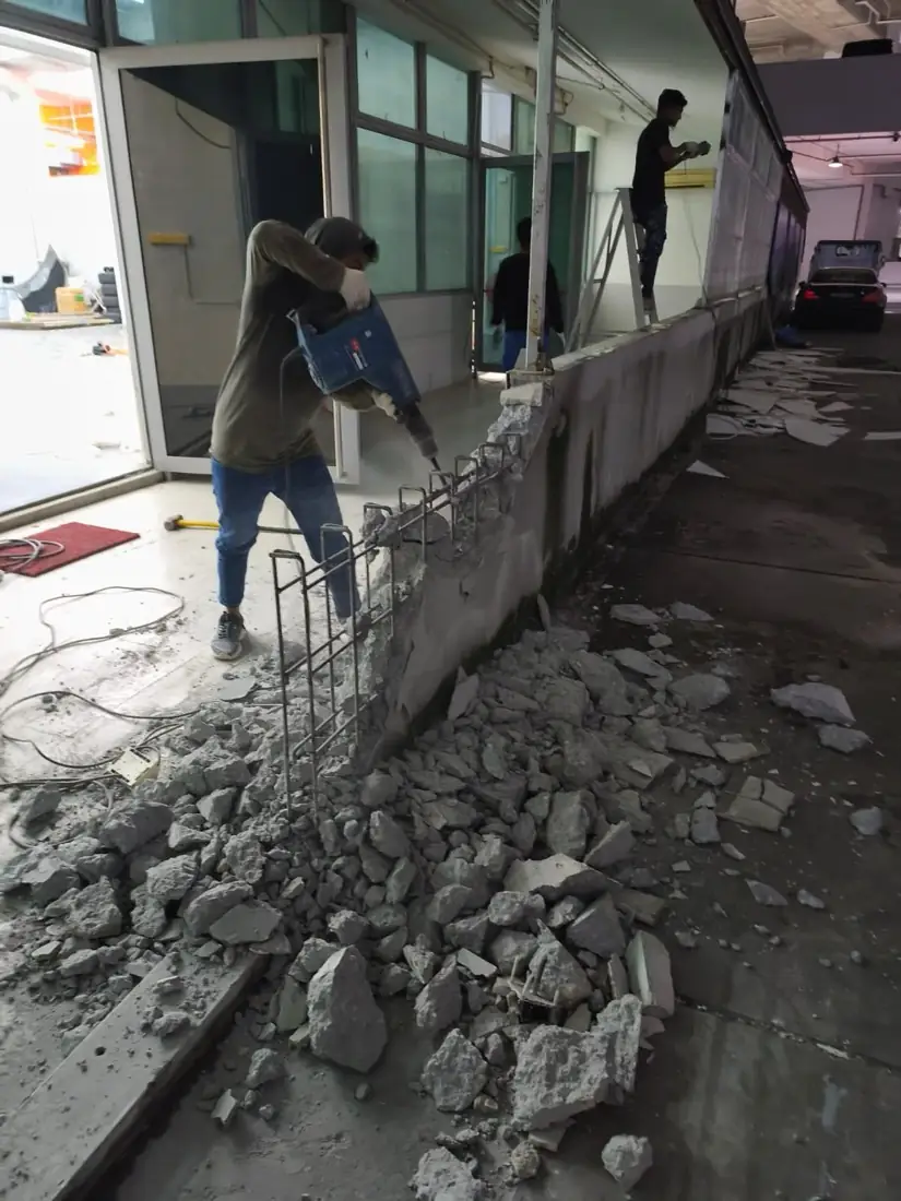 Worker hacking a low wall with debris on the floor