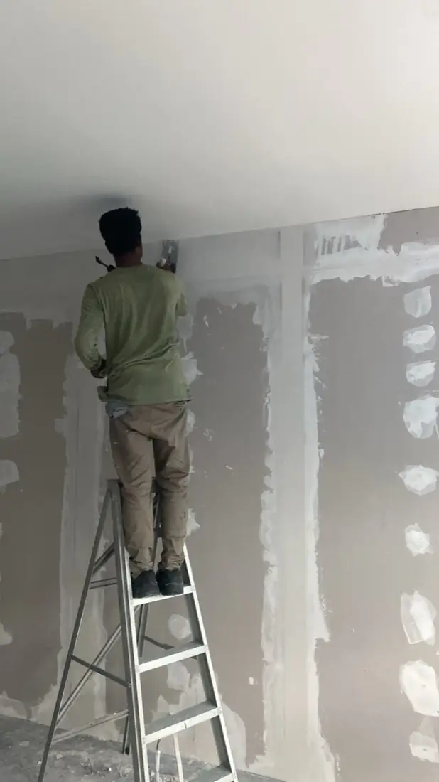 Worker skim-coating a wall on a ladder